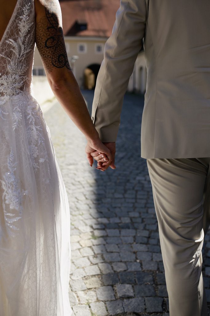 Händchen haltendes Brautpaar auf einem gepflasterten Weg.