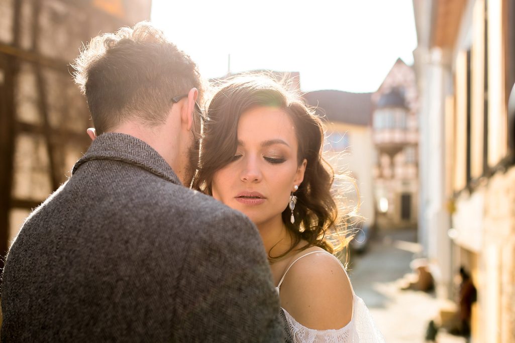 Ein Brautpaar steht im Freien vor einer Altstadt Kulisse und umarmt sich. Sonnenlicht scheint.