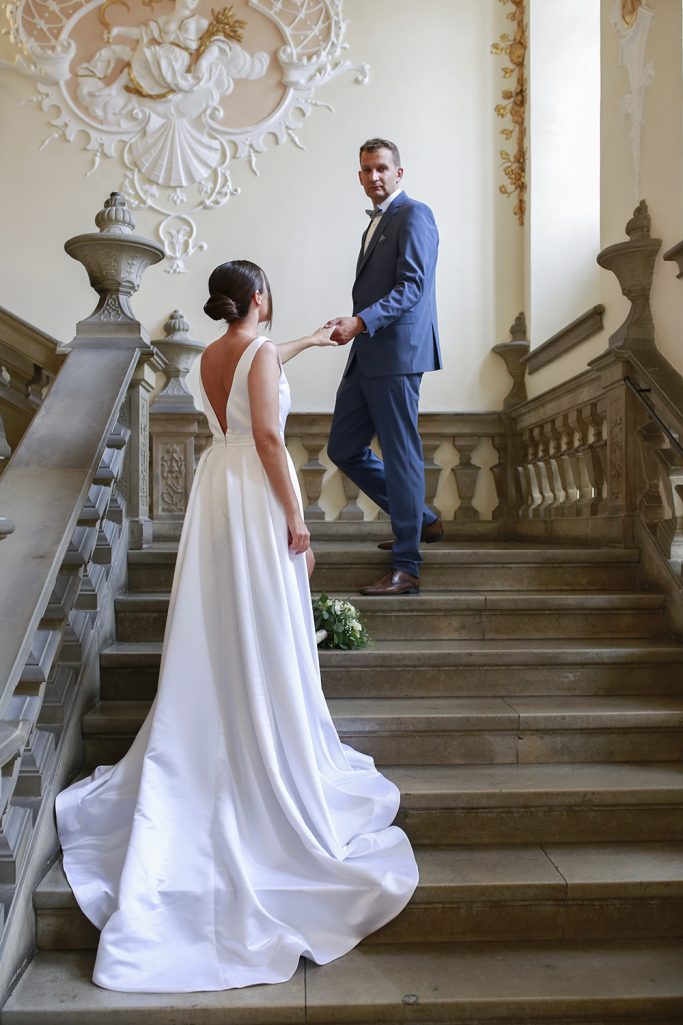 Hochzeitspaar auf einer Treppe. Der Bräutigam schaut die Braut an und hält liebevoll ihre Hand.