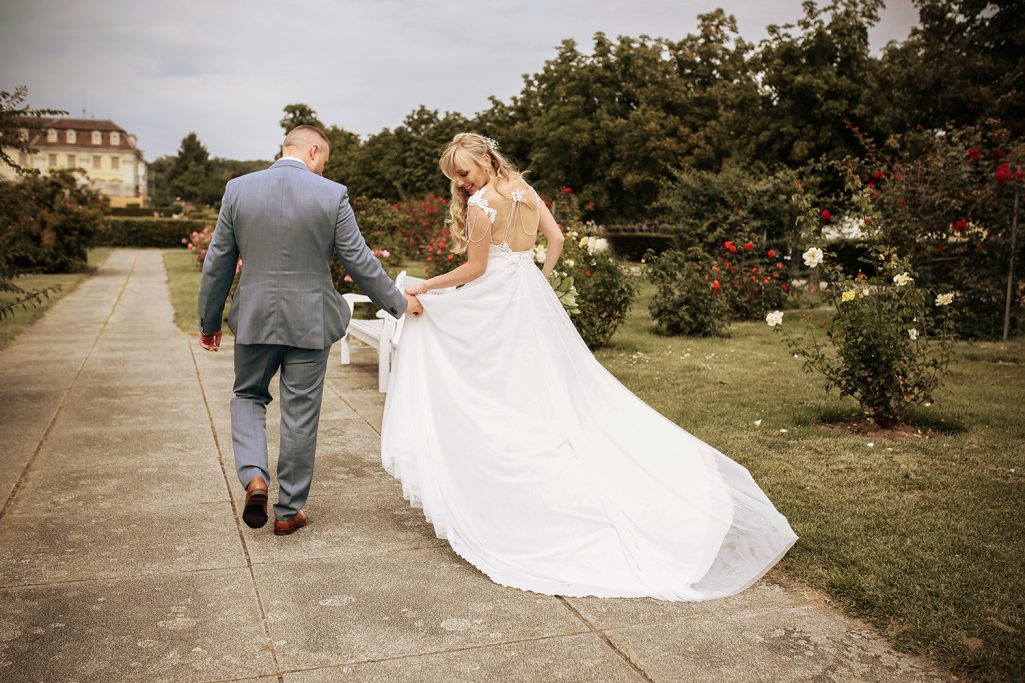 Ein Brautpaar geht Hand in Hand auf einem Weg durch einen blühenden Garten.