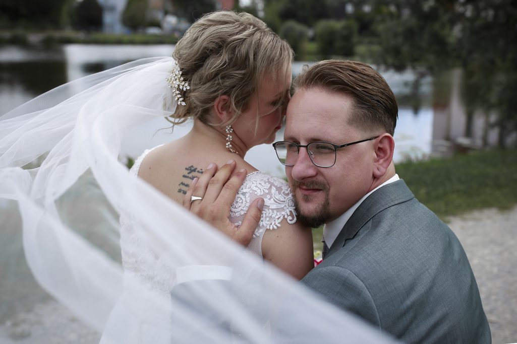 Braut und Bräutigam posieren liebevoll am Wasser, umgeben von einem Schleier.