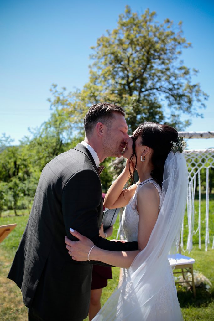 Ein Brautpaar küsst sich unter blauem Himmel während der Zeremonie im Freien.