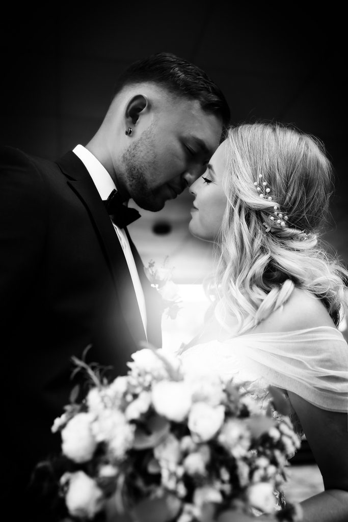 Ein Brautpaar steht sich nahe, küsst sich zärtlich, umgeben von Blumen.
