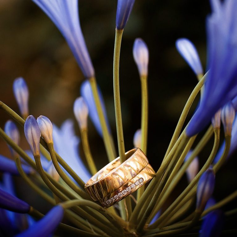 Ein goldener Ehering liegt zwischen blauen Blütenblättern.
