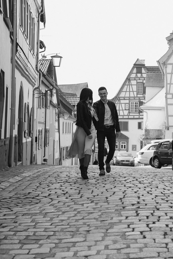 Paar spaziert auf einem Kopfsteinpflasterweg zwischen historischen Gebäuden.