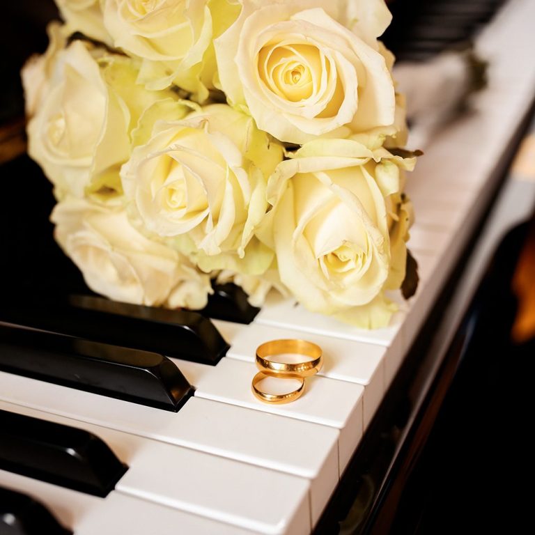 Weiße Rosen und Eheringe liegen auf einem Klavier.