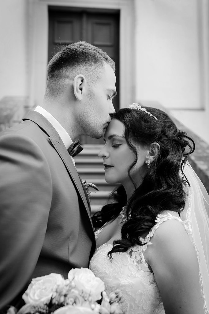 Hochzeitspaar in einem innigen Moment. Bräutigam küsst liebevoll die Stirn der Braut. Die Braut genießt den emotionalen Moment.