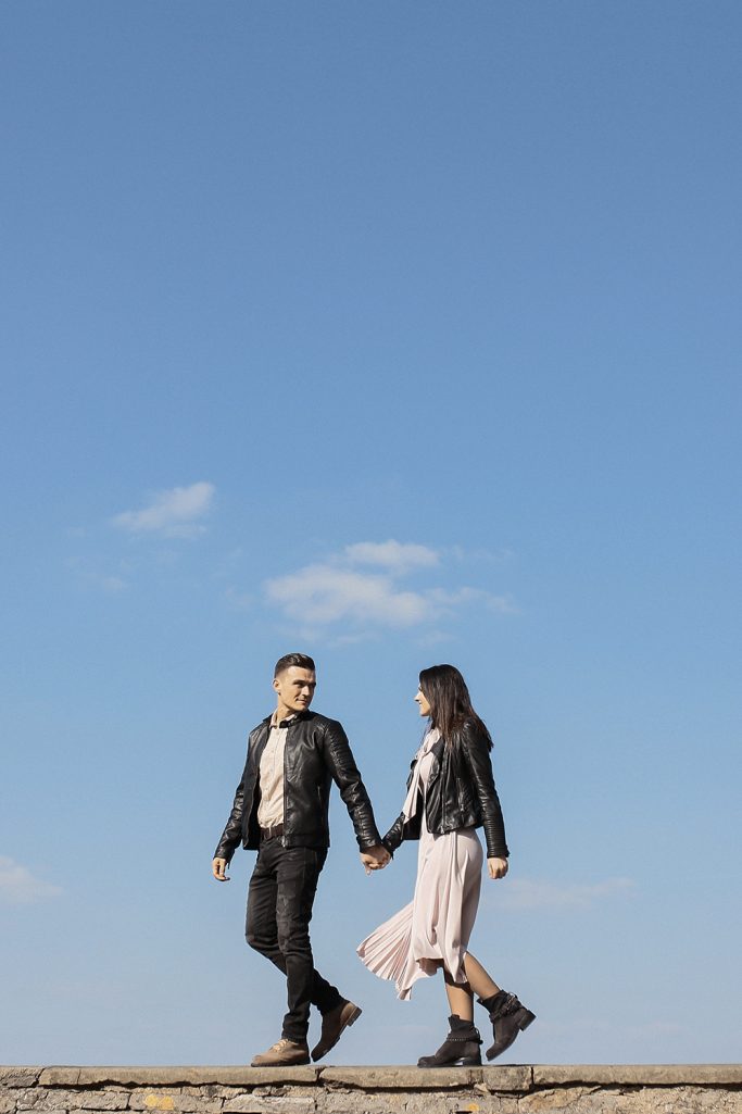 Ein Paar geht Hand in Hand unter blauem Himmel und schaut sich dabei an.