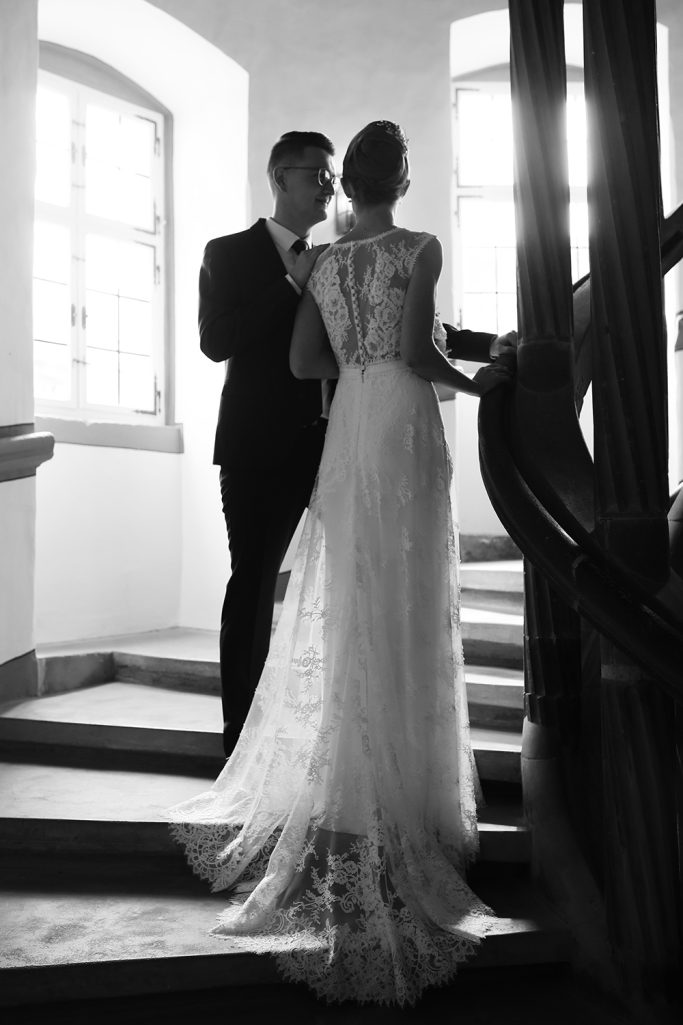 Brautpaar steht an einer Treppe, romantische Atmosphäre in Schwarz-Weiß.