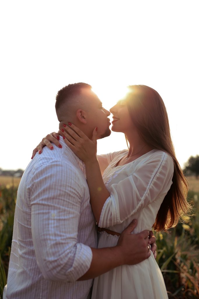 Paar in romantischer Umarmung und dabei, sich zu küssen. Steht in einem Sonnenblumenfeld, beleuchtet von Sonnenlicht im Hintergrund.