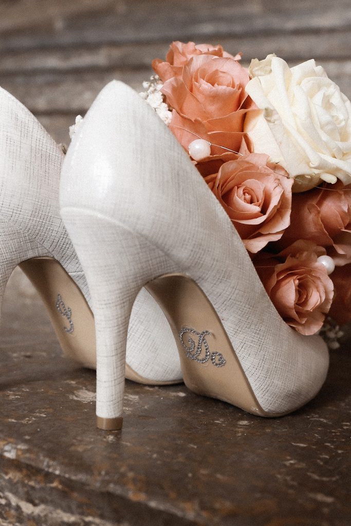 Elegante, weiße Brautschuhe neben einem Strauß aus Rosen in sanften Farben.
