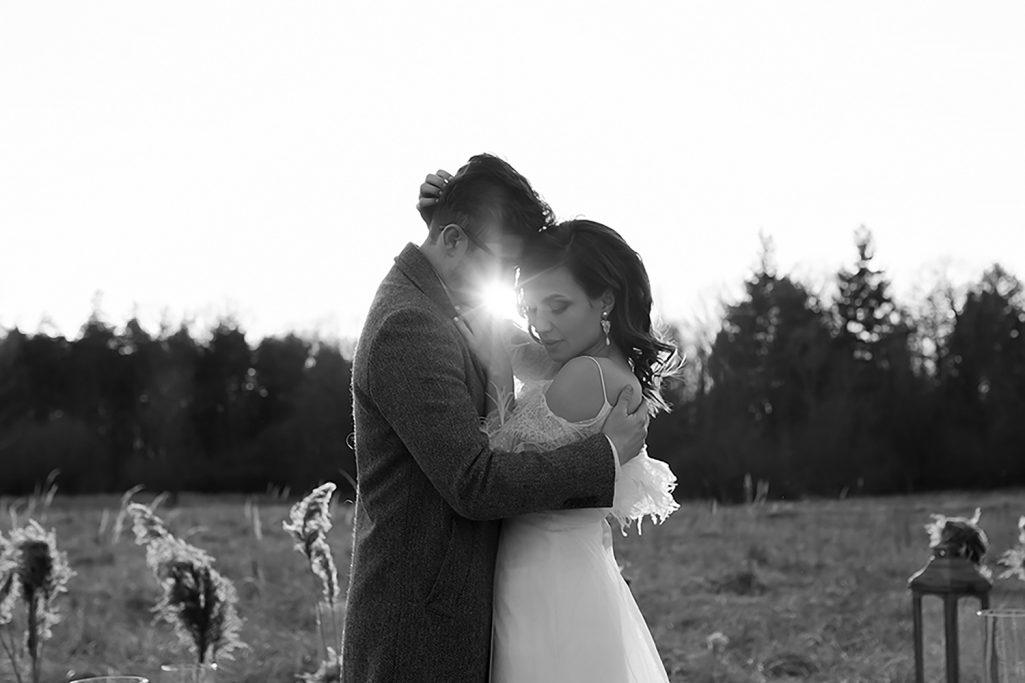 Ein Paar umarmt sich liebevoll vor einer malerischen Landschaft in Schwarz-Weiß. Zwischen den beiden scheint die Sonner hervor.