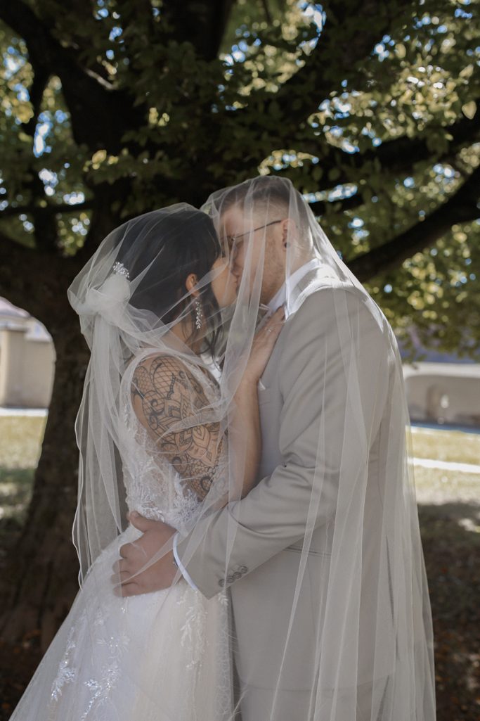 Ein Brautpaar umarmt und küsst sich unter einem Baum.