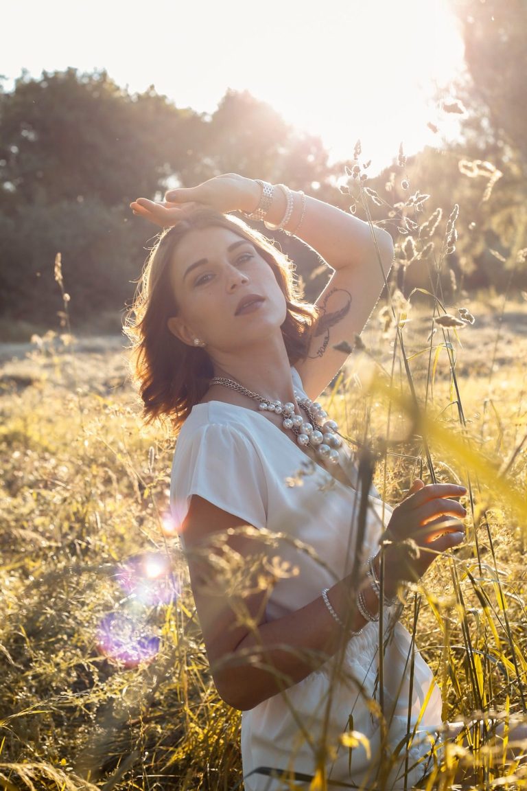 Frau mit kurzem Haar posiert in einem goldenem Feld, Sonnenstrahlen im Hintergrund.