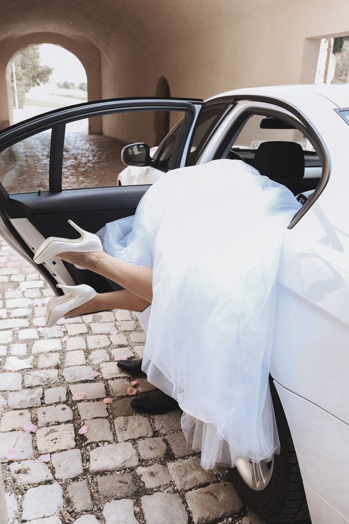 Braut in einem weißen Kleid und hohen Schuhen steigt in ein Auto.