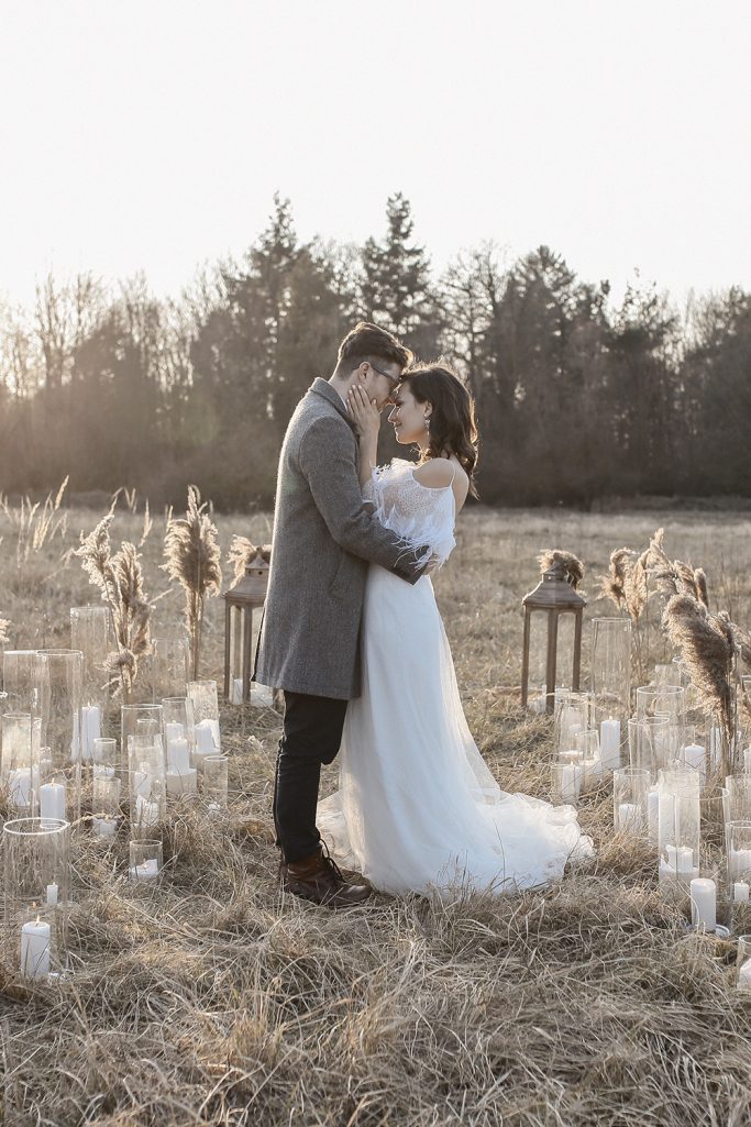 Brautpaar umarmt sich auf einer Wiese in einer Lichtung mit Kerzen und Pflanzen, im Hintergrund Bäume.