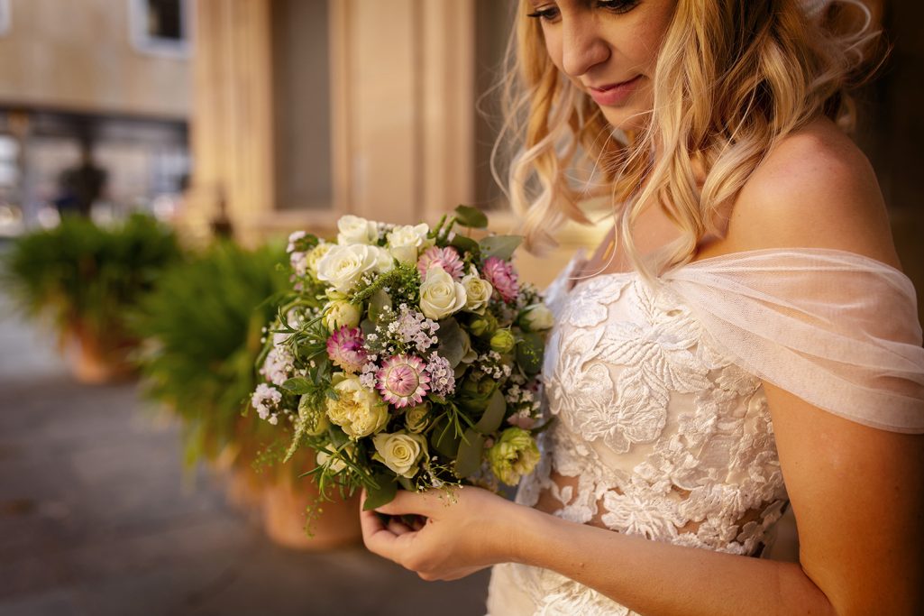 Braut mit einem Blumenstrauß aus Rosen und Grünpflanzen in einem romantischen Ambiente.