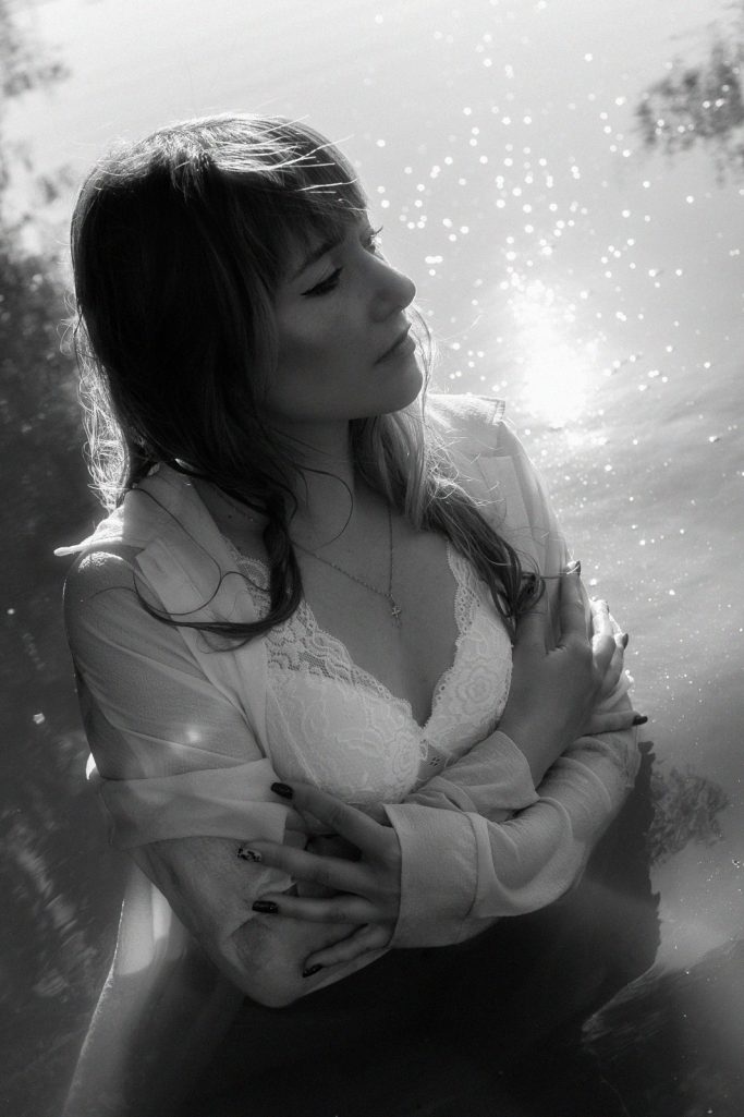 Junge Frau in einem Weißen Oberteil, nachdenklich im Wasser, monochromatisches Bild.