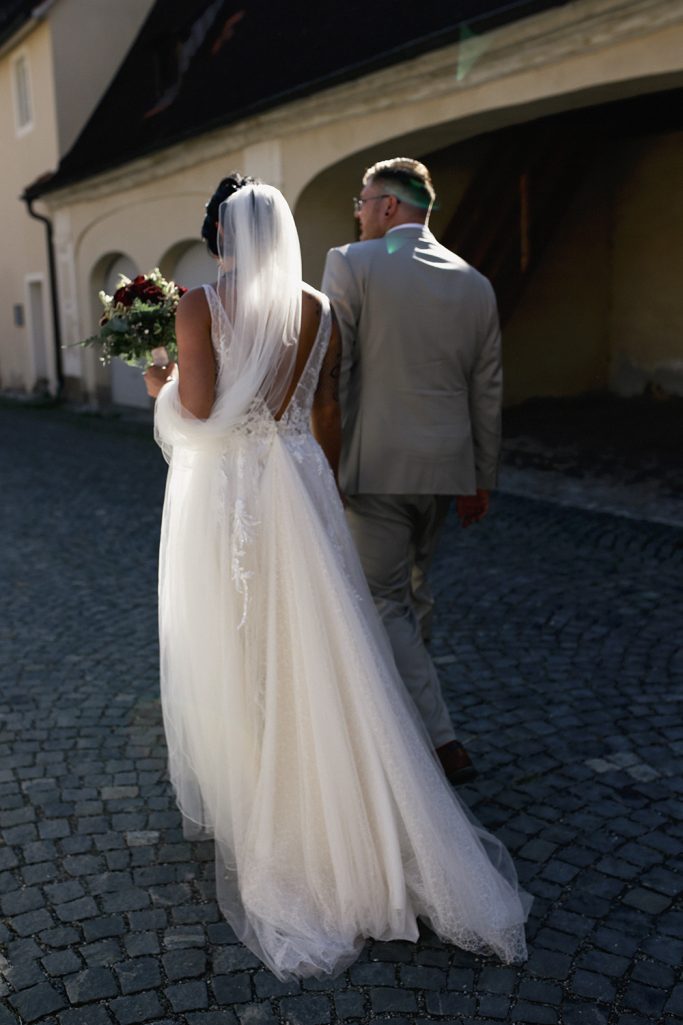 Braut und Bräutigam gehen Hand in Hand einen gepflasterten Weg entlang.