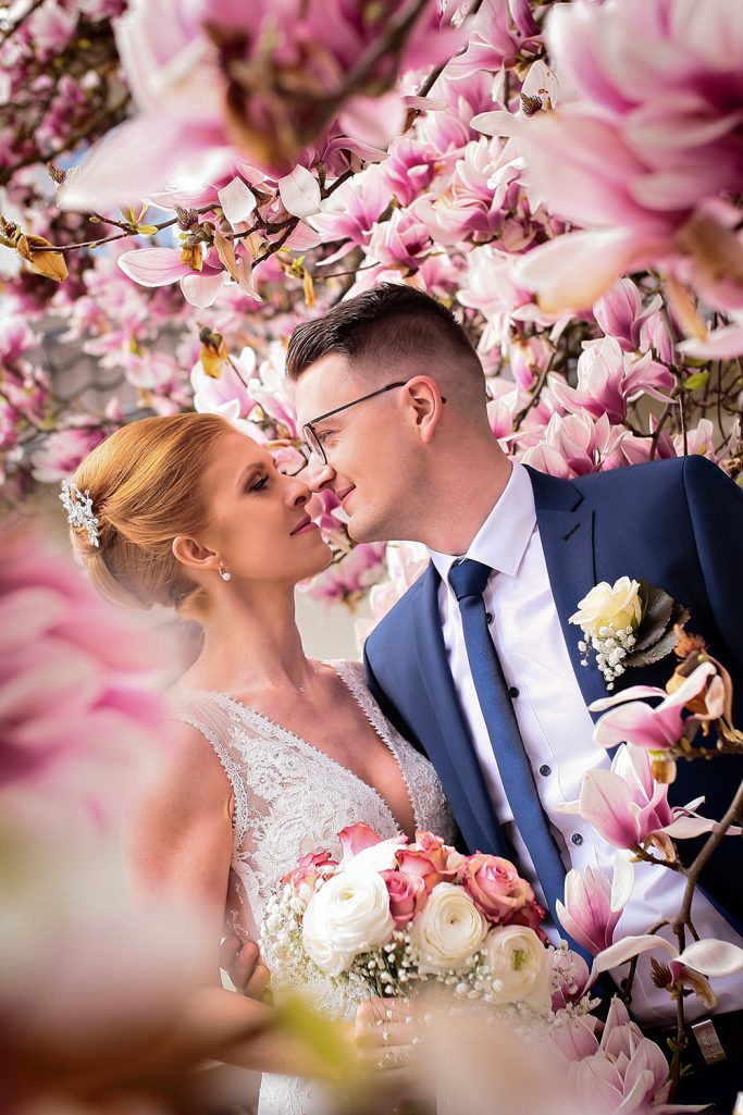 Brautpaar schaut sich romantisch vor blühenden Magnolien an.